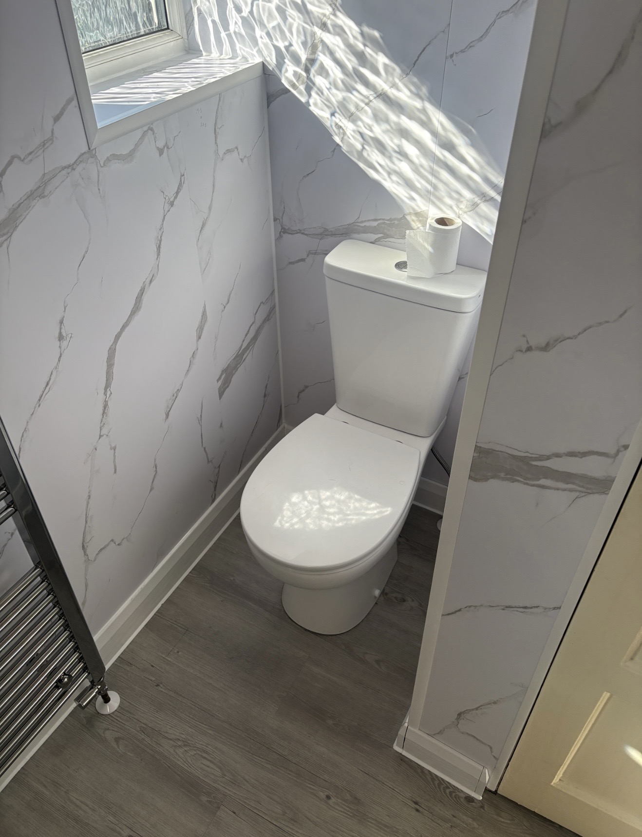 Finished bathroom toilet area with new flooring, wall panels and heated towel rail