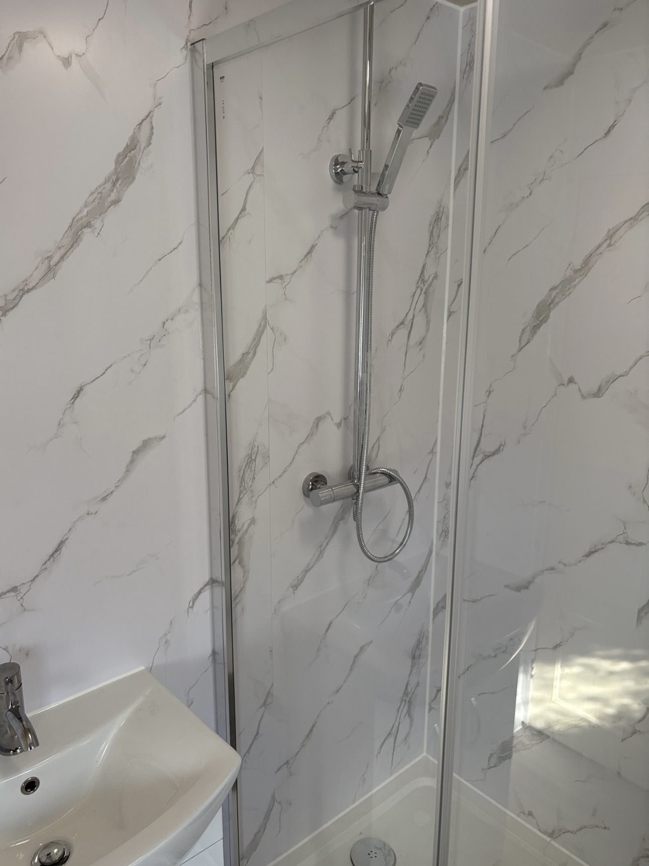 Completed shower enclosure with marble-effect wall panels in the refurbished bathroom