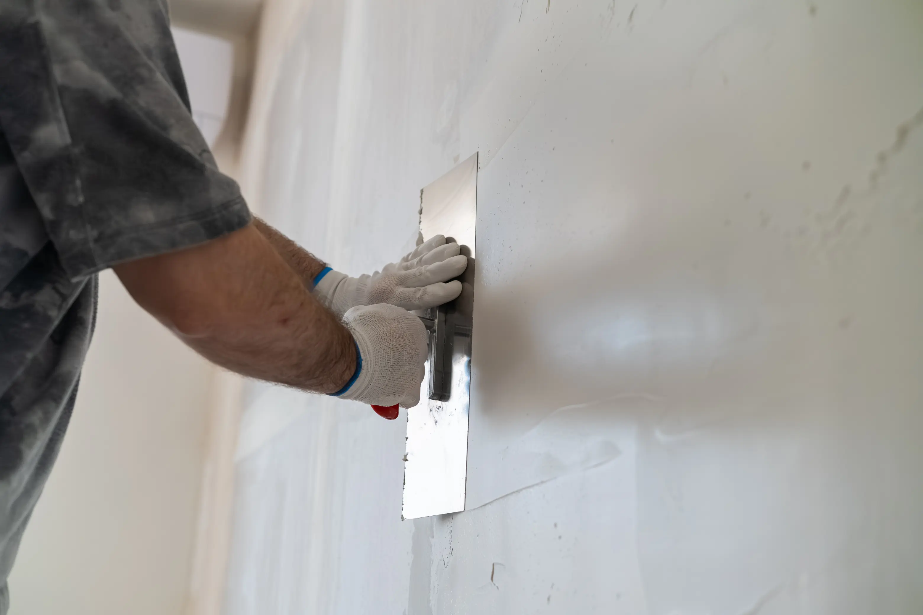 A plasterer smoothing a fresh skim coat onto a wall with a steel trowel